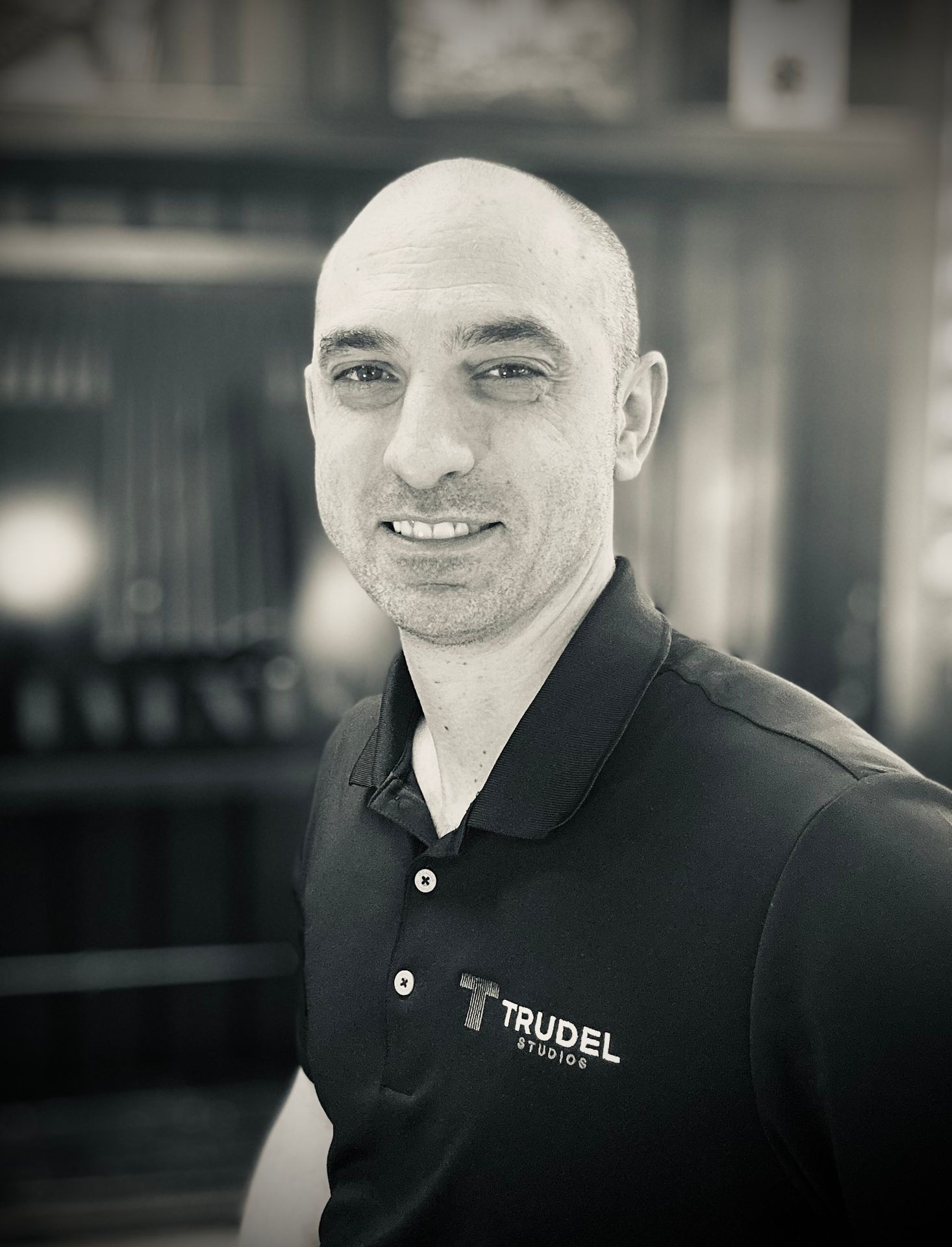 Individual wearing a black polo shirt with Trudel Studios logo standing indoors with blurred background.